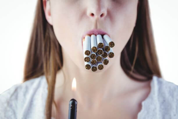 Frau, die vom Rauchen nicht genug kriegen kann und mehrere Zigaretten im Mund hat